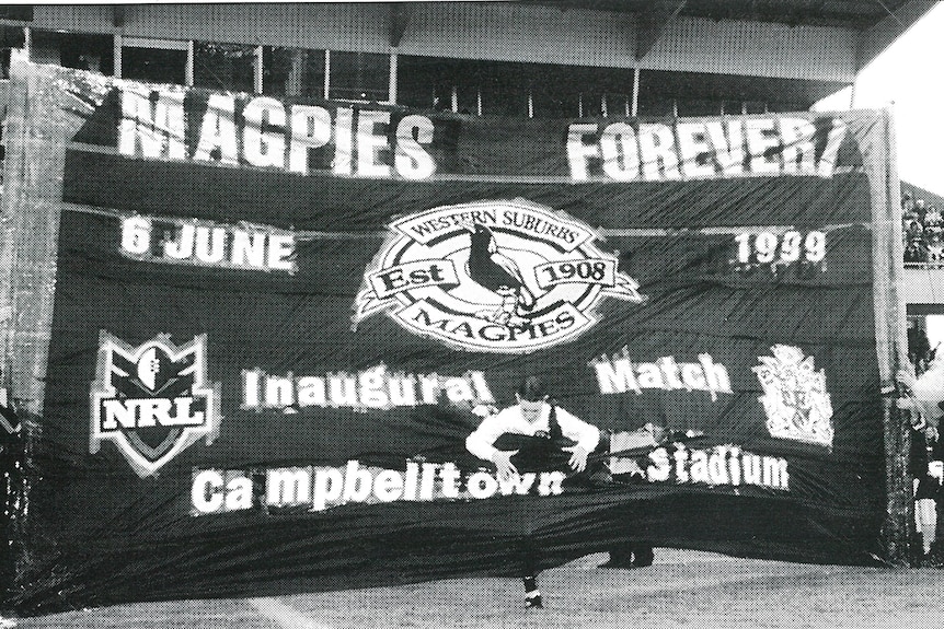 A man runs through a banner onto the field for a rugby league match