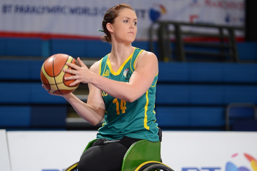 A female wheelchair basketballer is playing and looks to pass the ball.