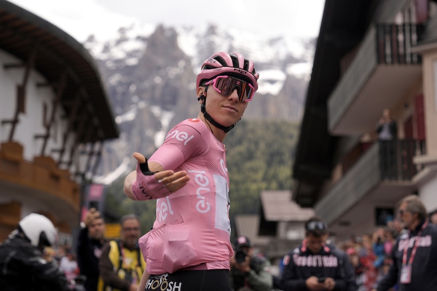 Tadej Pogacar turns to the camera with mountains behind him