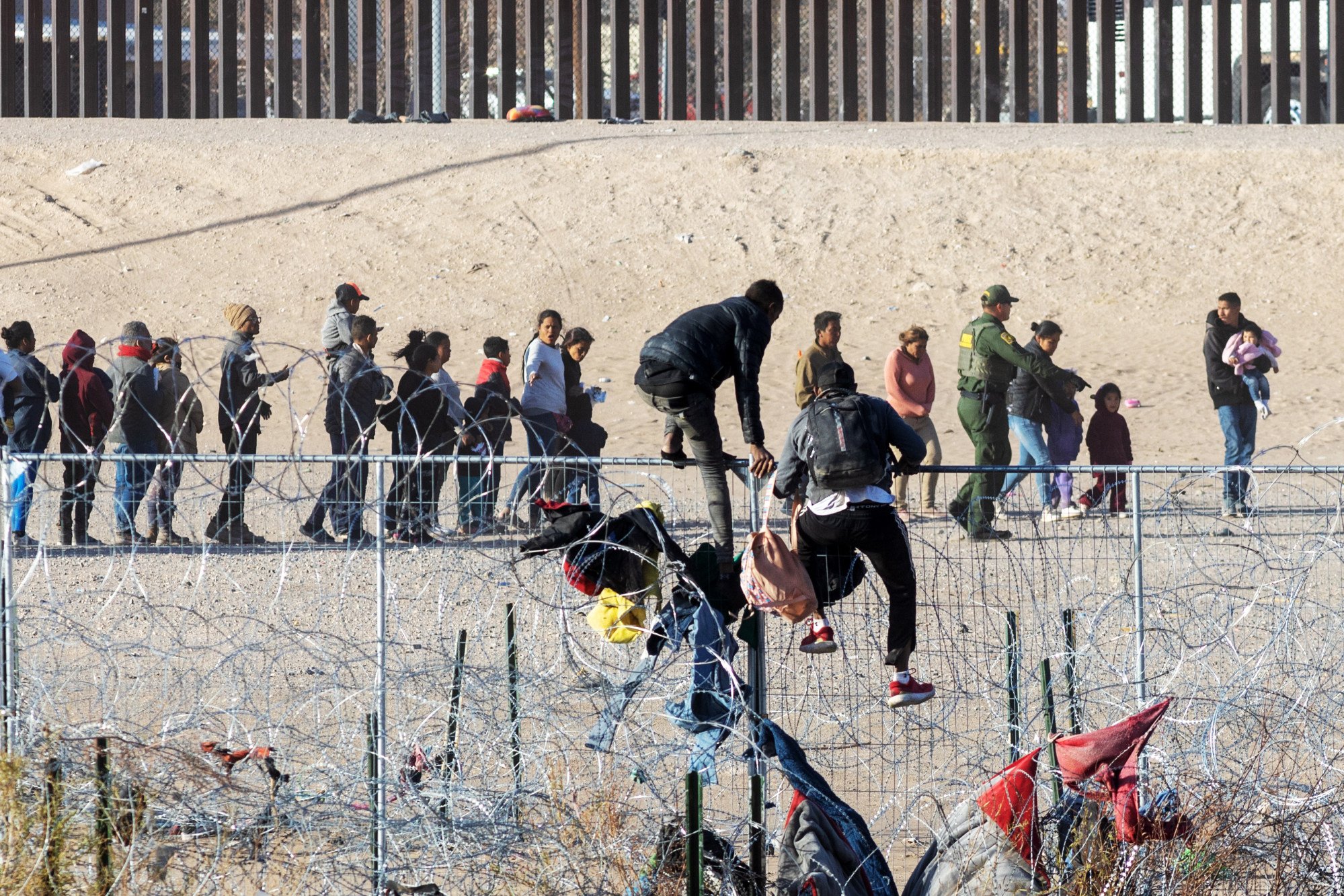 Two men scale the cyclone fence installed by the Texas National Guard, as hundreds of migrants queue up along the border wall dividing Mexico and the United States. Photo: dpa