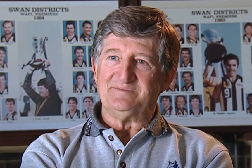 A headshot of John Todd talking during a TV interview, sitting in front of photo frames showing Swan Districts football teams.