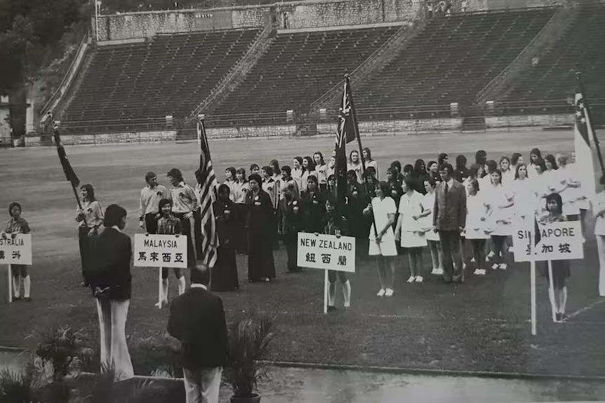 A black and white photo of women's soccer teams lining up behind signs saying their countries before a tournament