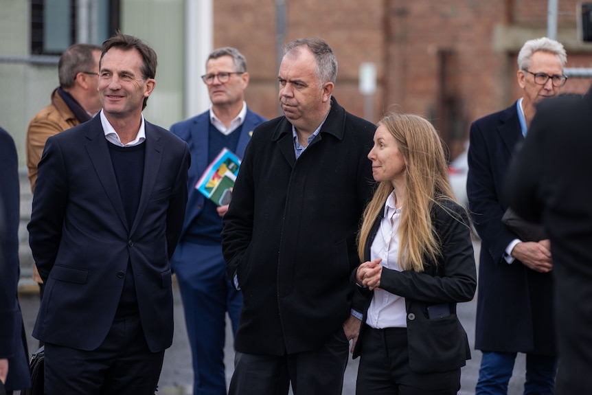 2 men and a woman standing outside in a carpark.