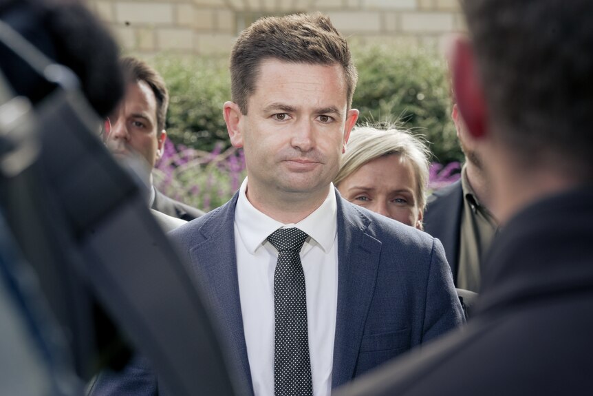 Group of people chatting on green lawn with cameramen around.