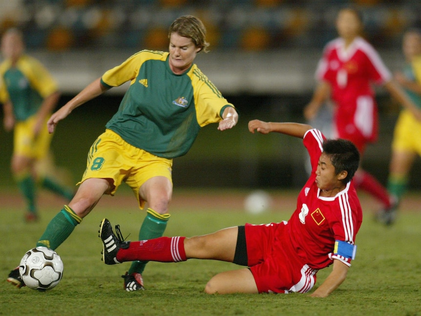 Two female soccer players, one wearing green and yellow and the other wearing red and white, during a match