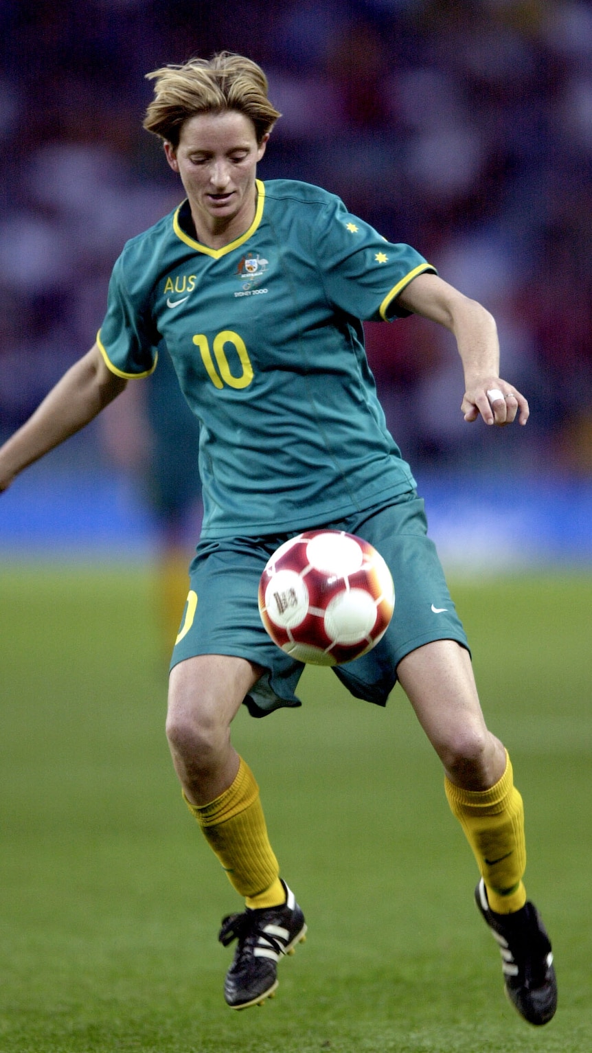 A female soccer player wearing green and yellow controls the ball during a game