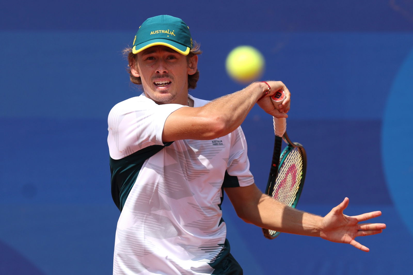 A tennis player wearing a white shirt and green hat hits a tennis ball.