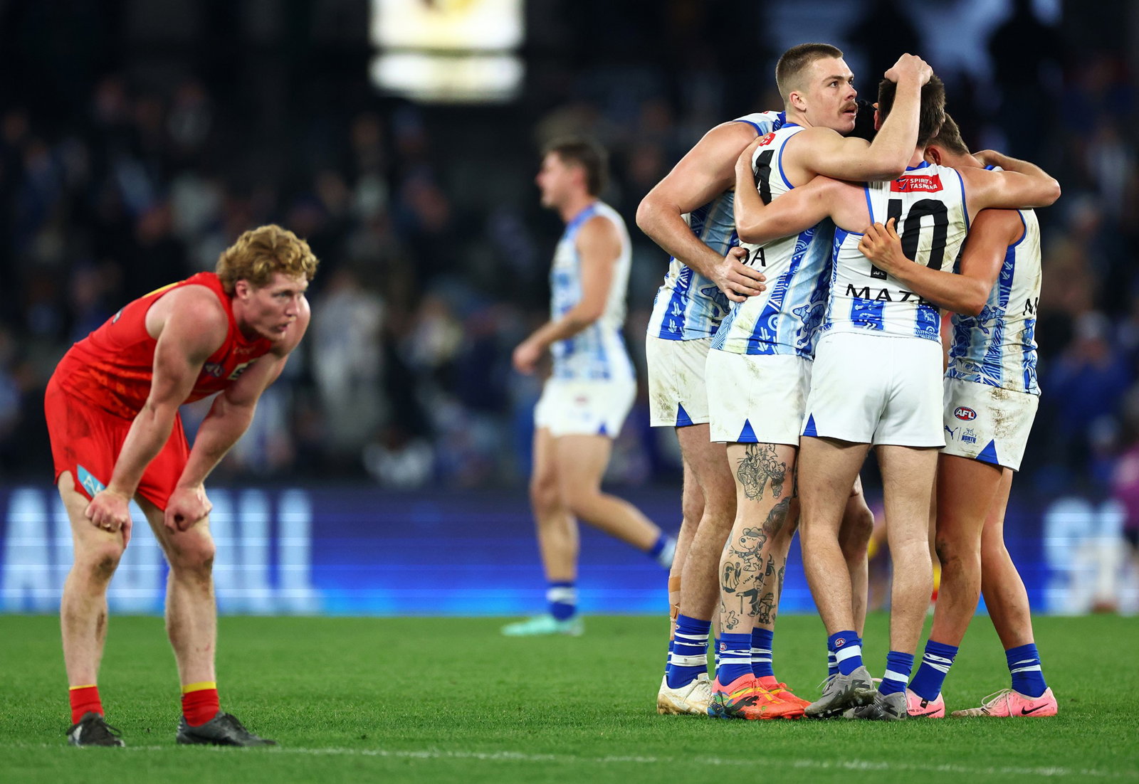 Kangaroos players celebrate at the final siren as Suns star Matt Rowell wonders what might've been