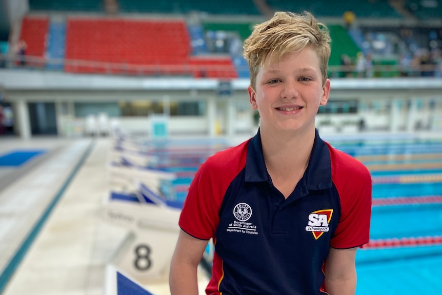 blonde boy sits on diving podium smiling to camera