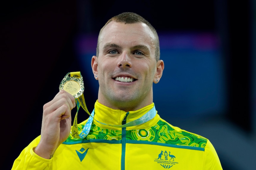 Australian swimmer Kyle Chalmers smiles as he holds his gold medal up on the podium at the Commonwealth Games.