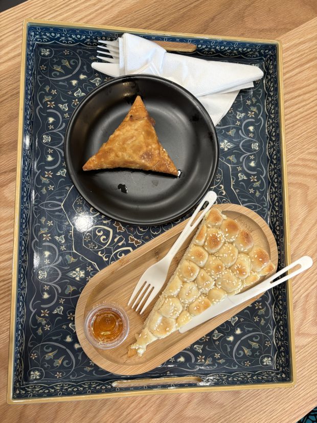 a tray of food, including a triangle sambusa on a black plate and a long triangular slice of bread on a wooden plate