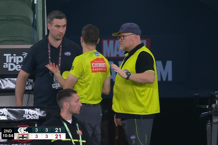 AFL umpire in high vis t-shirt with a blood-covered hand.