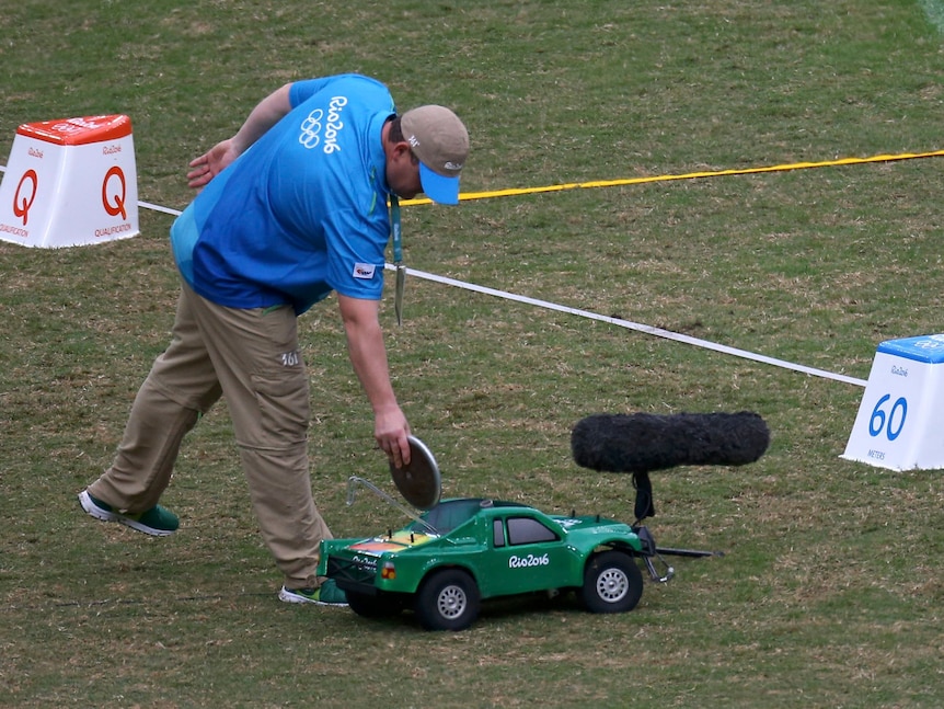 An official leans over to place a discuss in the back of an RC that resembles a green pick-up truck 