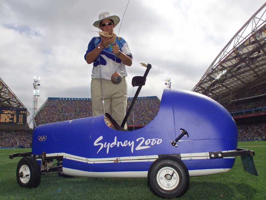 An Olympics official cleans a hammer as she stands in front of a blue RC