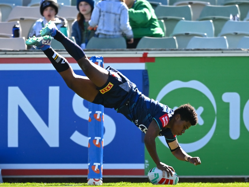 A Cowboys NRLW player dives full length in the air and reaches down from a height to plant the ball down for a try.