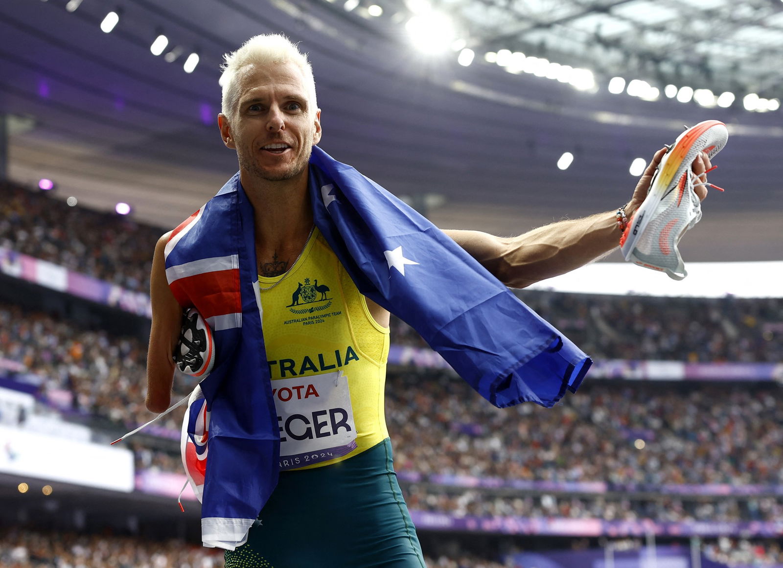 Australian Paralympian Michael Roeger has an Australian flag around his next and one arm outstretched holding a shoe.