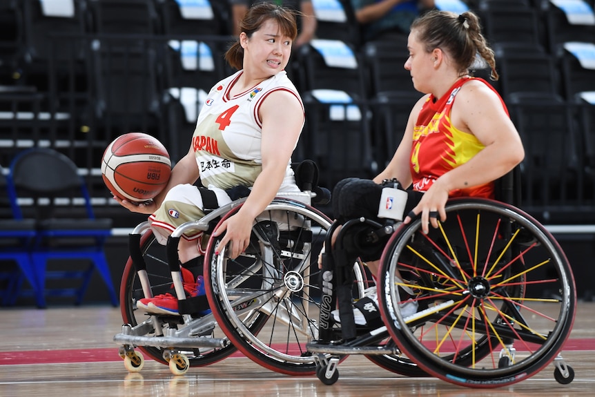 A female wheelchair basketballer from Japan looks to pass the ball as a Spanish player defends.