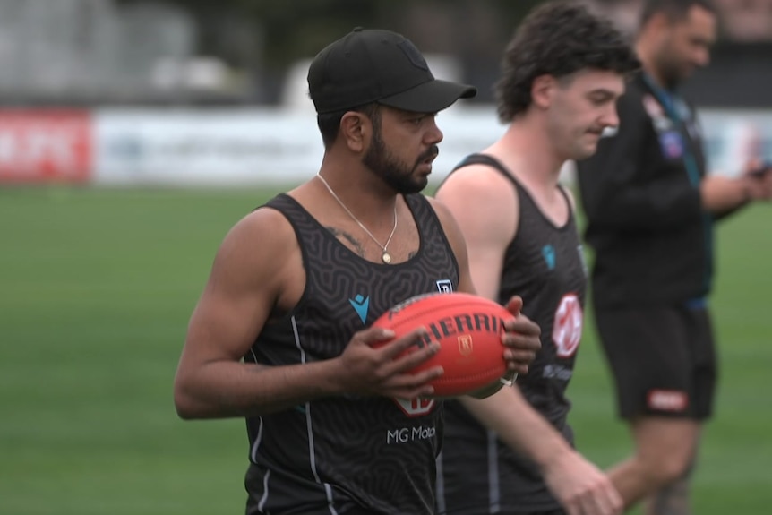 Willie Rioli holding a footy on field with other players