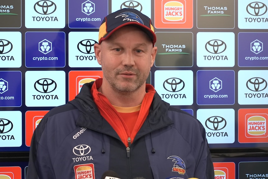 Matthew Nicks in Crows sportgear in front of brand sponsorship banner speaking with media
