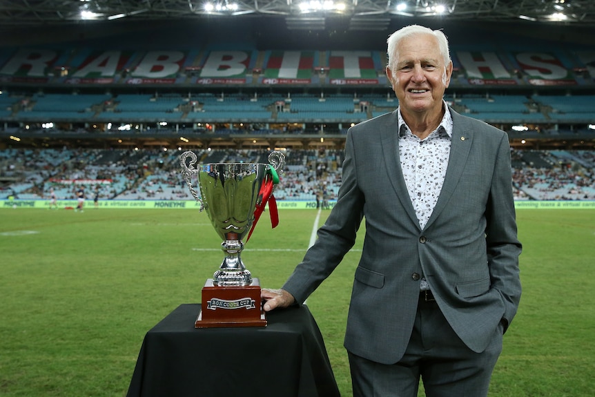 NRL Immortal Ron Coote standing at Stadium Australia with a trophy, posing for a picture