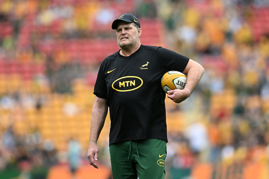 Springboks coach Rassie Erasmus holding a rugby ball under his arm during team warm-ups