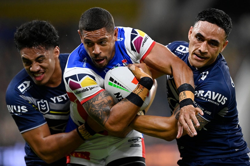 Dane Gagai of the Knights is tackled by Murray Taulagi and Valentine Holmes of the Cowboys