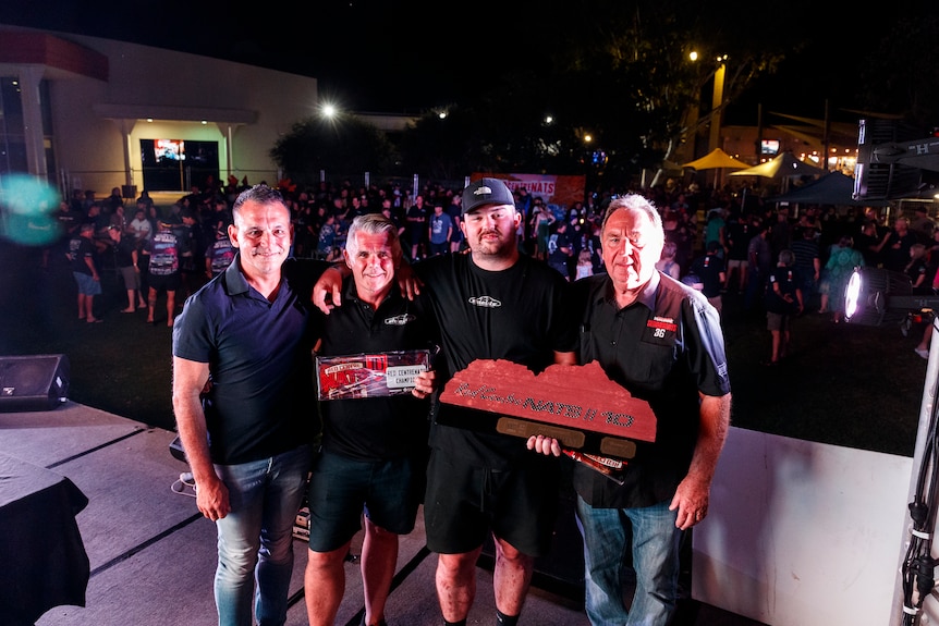 Four men stand with award in front of crowd