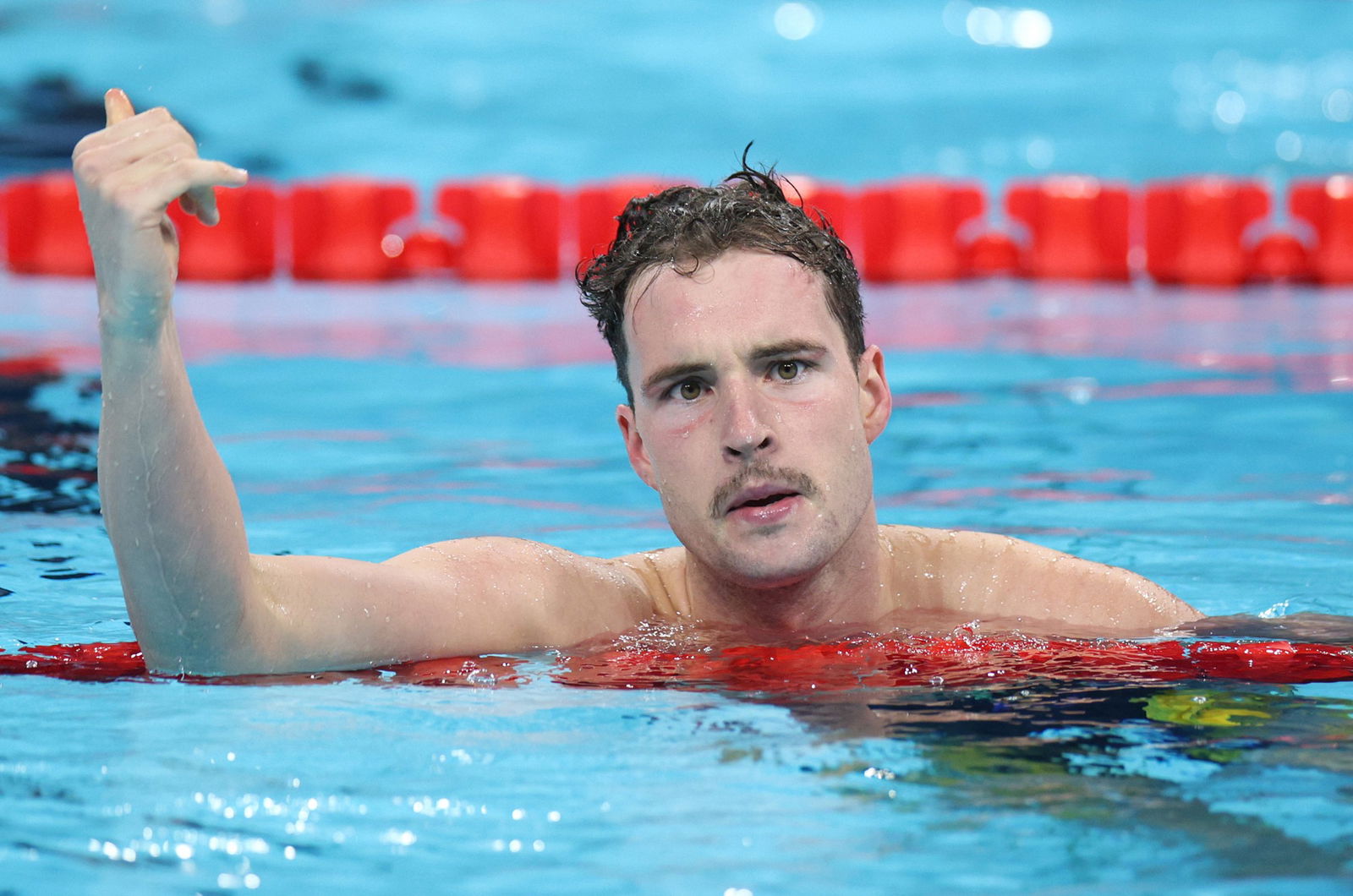 Australian Para swimmer Ben Hance rests on the lane rope and has an arm raised in the air.