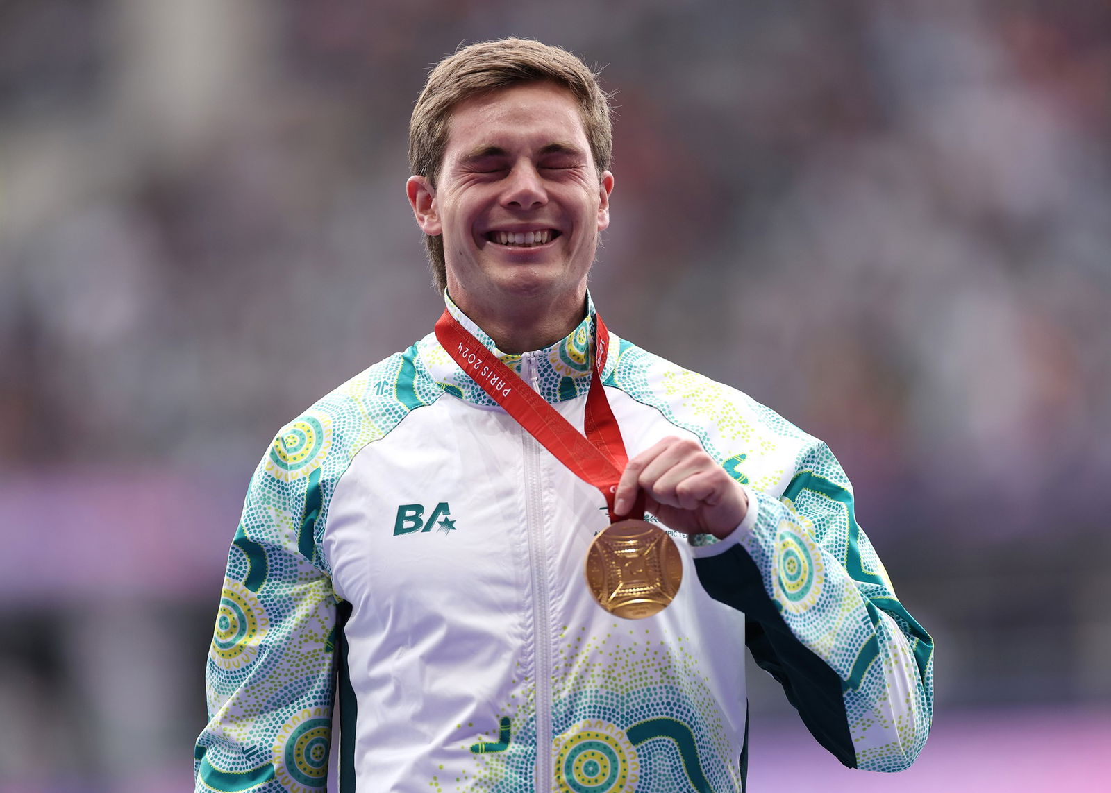 Australian Paralympian James Turner stands on the podium with his eyes closed and a smile holding his gold medal.