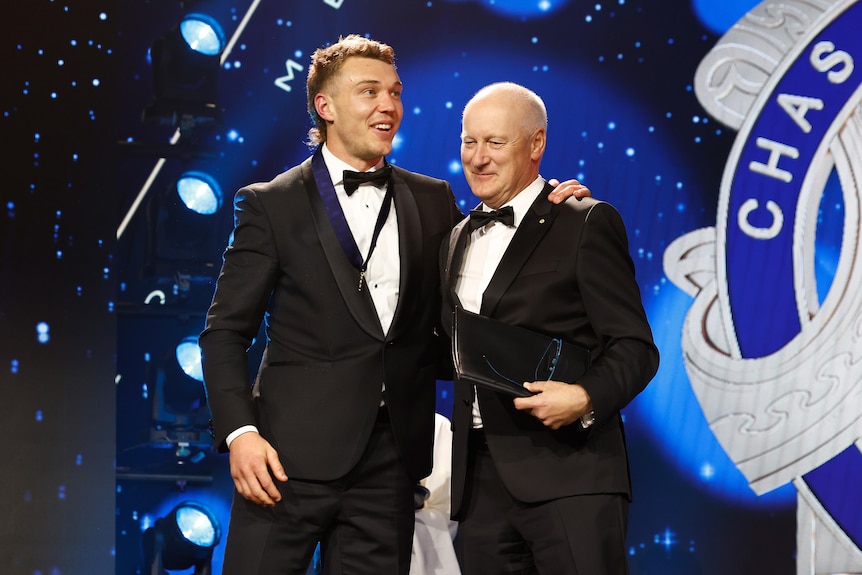 Two men in suits pose, one with a medal around his neck.