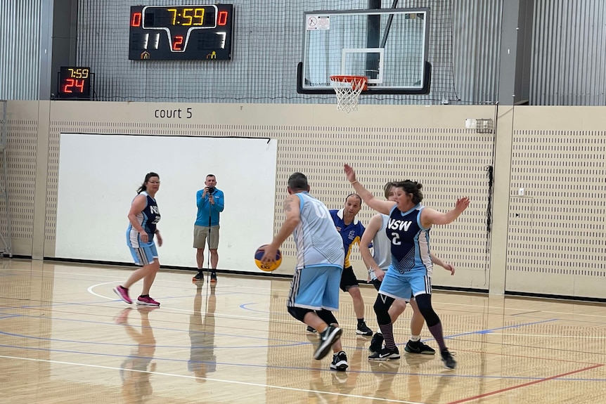 A group of people play basketball at an indoor court.