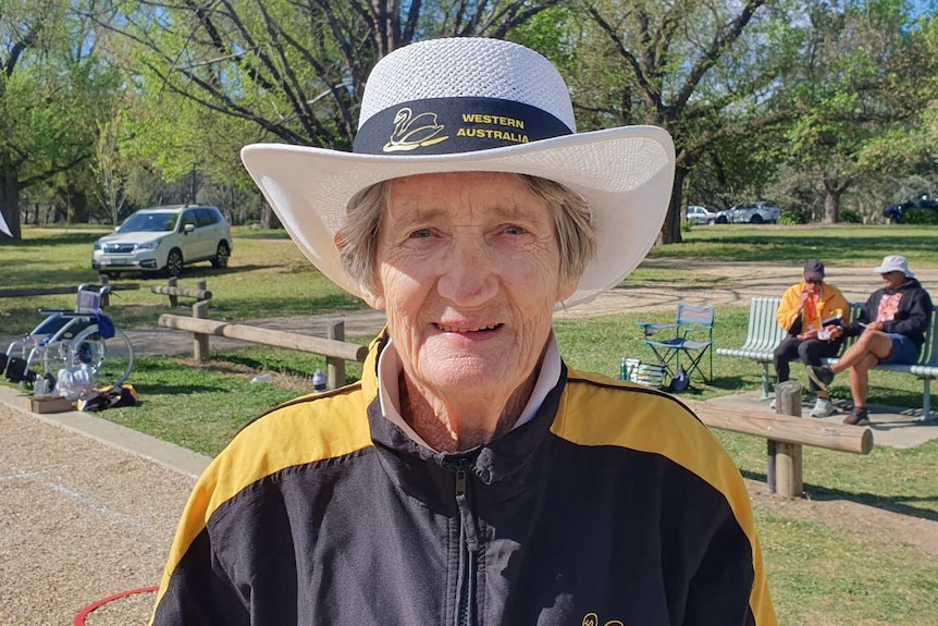 A woman stands outside wearing a white, wide-brim hat.