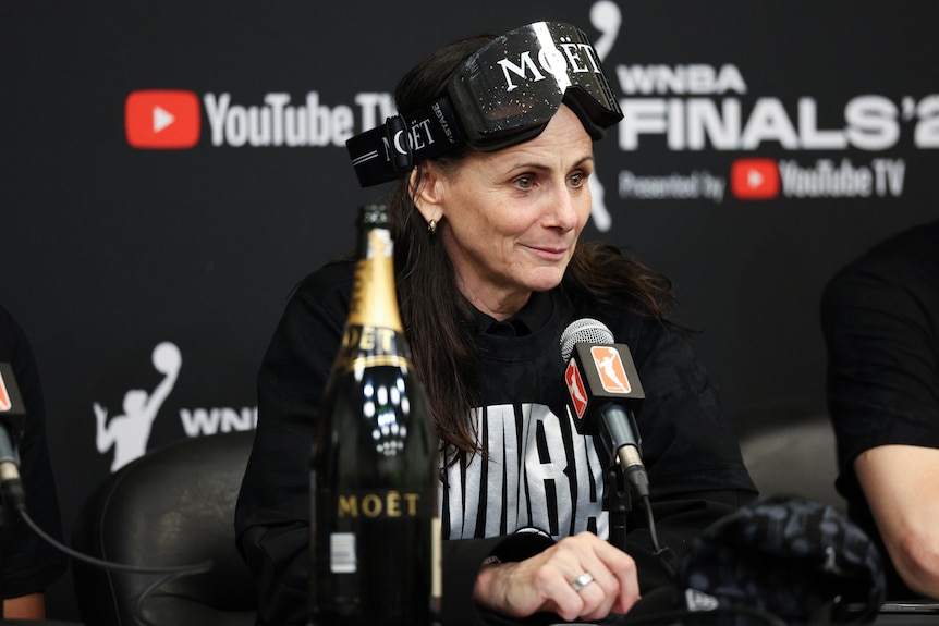New York Liberty coach Sandy Brondello wears ski goggles as she sits at the podium after winning the WNBA Finals.