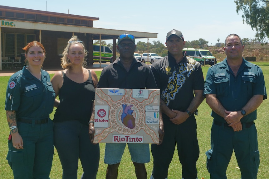Three men and two women, f five people getting a photo in a line on a footy oval. Two wear paramedics uniform.