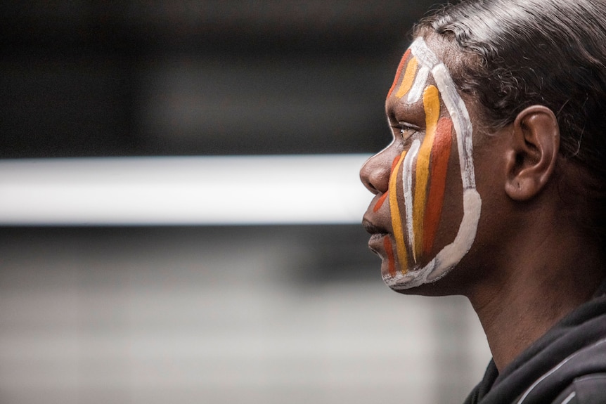 A side profile of an Indigenous woman with a painted face.