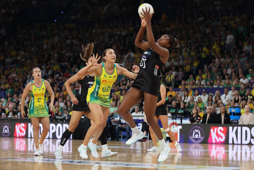 A New Zealand netballer jumps with hands extended to catch the ball during a netball test against Australia.