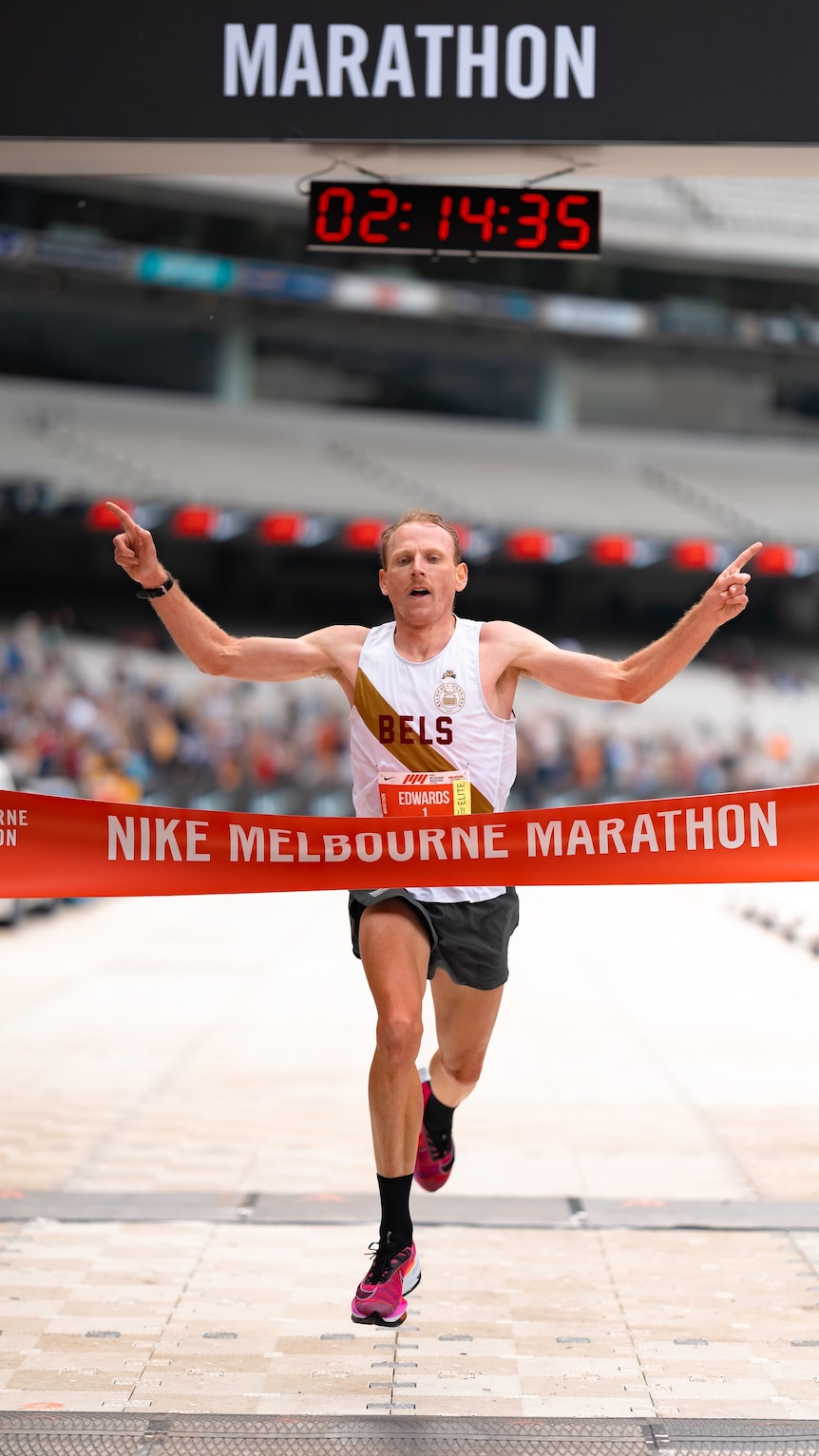 Reece raises his arms as he crossed the Melbourne Marathon finish line, with the time 02:14:35 on a screen above him. 