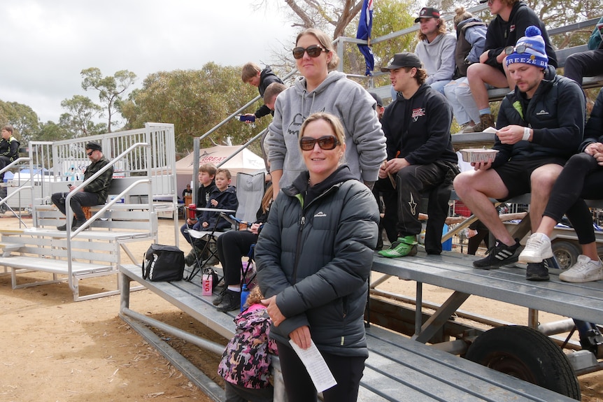 A woman wearing a black puffy jacket standing in front of a small grandstand