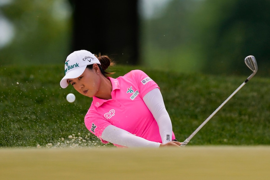 Australian golfer Minjee Lee, wearing a pink top, hits her ball out of a bunker