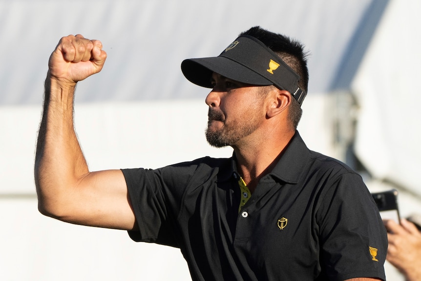 Jason Day punches the air woth his fist, celebrating with a crowd after victory on the 18th hole