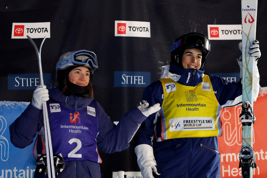 Jaelin Kauf shrugs as Jakara Anthony smiles and holds up her skis