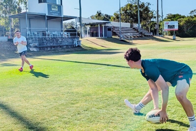 A young footballer passes a ball to his dad on a rugby league field.