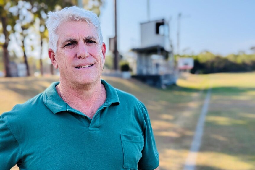 A mean wearing a green shirt standing on the sideline of a football field.