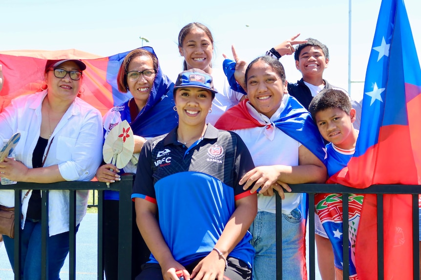 A Samoan rugby league player with her family, holding Samoan flags.