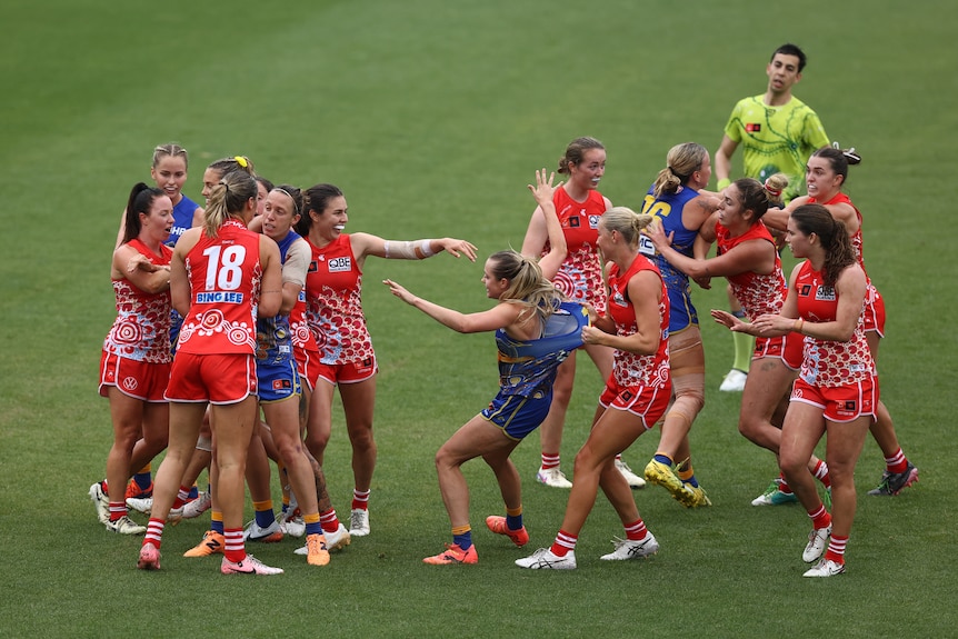A group of Sydney and West Coast AFLW players wrestle on the field during a break in play, 