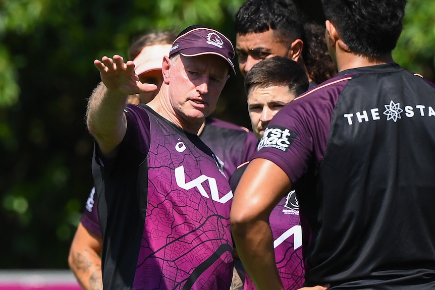 A Brisbane Broncos NRL coach points across the field as he speaks to a number of players.