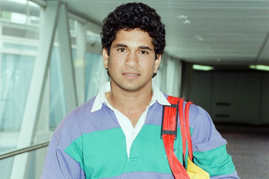 India cricketer Sachin Tendulkar stands in a hallway at an airport while carrying his bags.