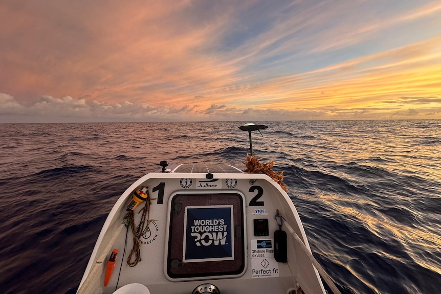 Looking out the front of a small row boat to the sun setting on open ocean