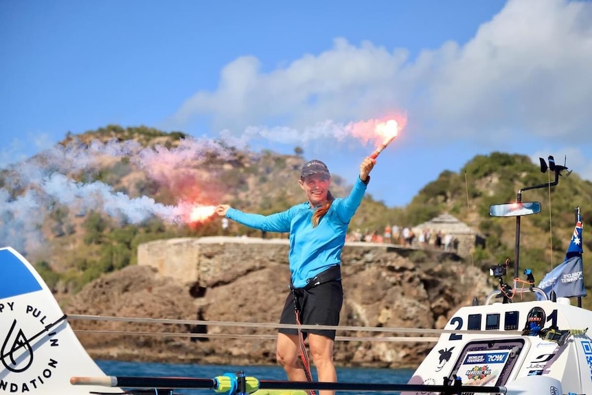 A woman standing on a small row boat holding a flare in each hand