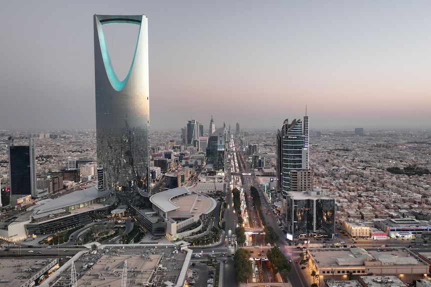 A wide shot from the air showing the cityscape of Riyadh in Saudi Arabia at dusk with one tall silver tower building